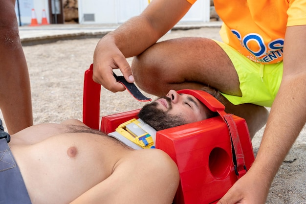 Personal médico de emergencia poniendo un collar médico a un hombre herido tirado en una playa