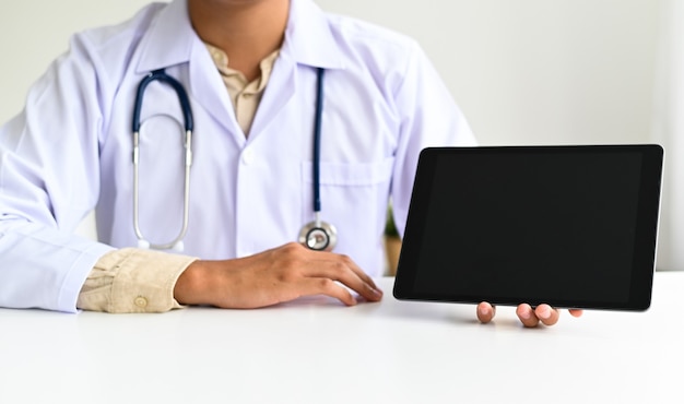 El personal médico usa batas sosteniendo una tableta digital en la mano, el médico usa una tableta en la mano para guiar a los pacientes en línea desde casa.