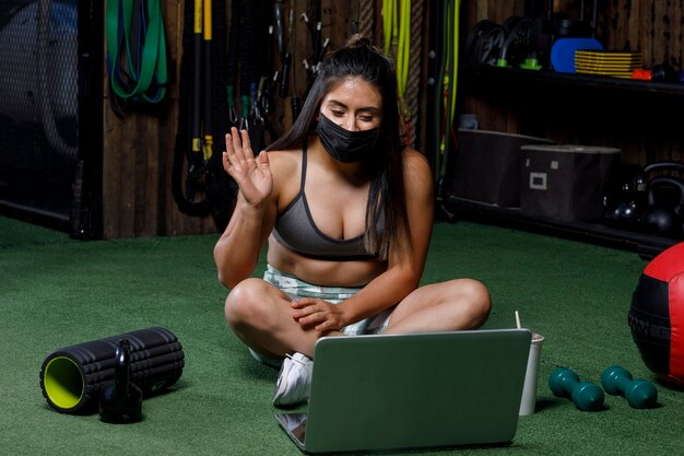 Personal trainer acenando na frente do computador depois de dar uma aula on-line tomando um drinque