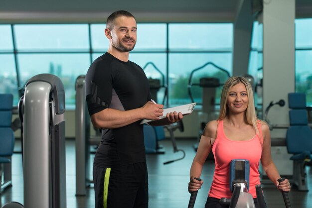 Personal Trainer, der jungen Frauen zeigt, wie man im Fitnessstudio wieder an der Maschine trainiert