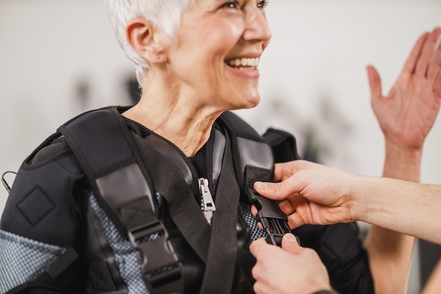 Personal trainer está ajudando uma mulher sênior com traje de vestir para EMS malhando na academia.