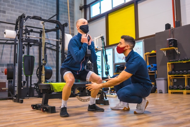 Personal Trainer im Fitnessstudio korrigiert die Kniebeugen des jungen Athleten bei der Coronavirus-Pandemie