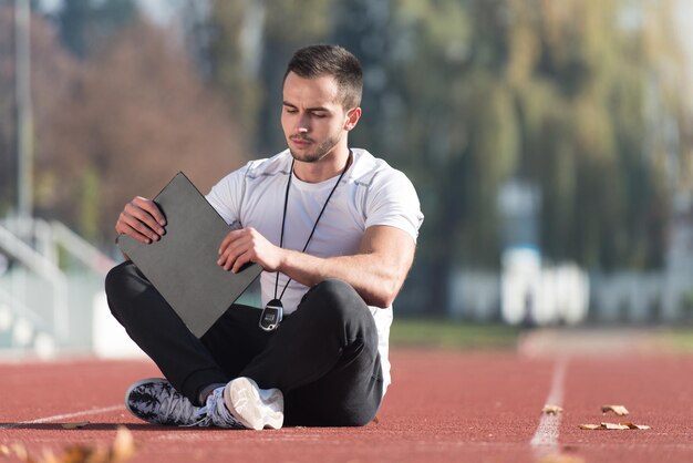 Personal Trainer im Sportoutfit macht sich Notizen auf der Zwischenablage im City Park Area Training und Training für ein gesundes Ausdauerkonzept im Freien