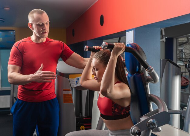 Foto personal trainer mann, der mit junger frau im modernen fitnessstudio arbeitet