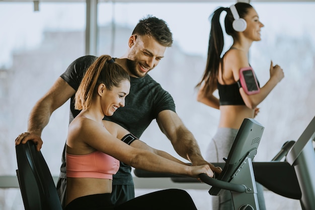 Personal Trainer mit junger Frau auf Fahrradmaschine im Fitnessstudio