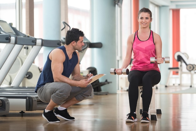 Personal trainer mostrando jovem mulher como treinar exercício de bíceps com halteres em um conceito de saúde e fitness