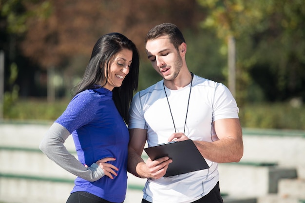 Personal Trainer toma notas enquanto a jovem se exercita na área do parque da cidade, treinando e exercitando para o conceito de estilo de vida saudável de resistência ao ar livre