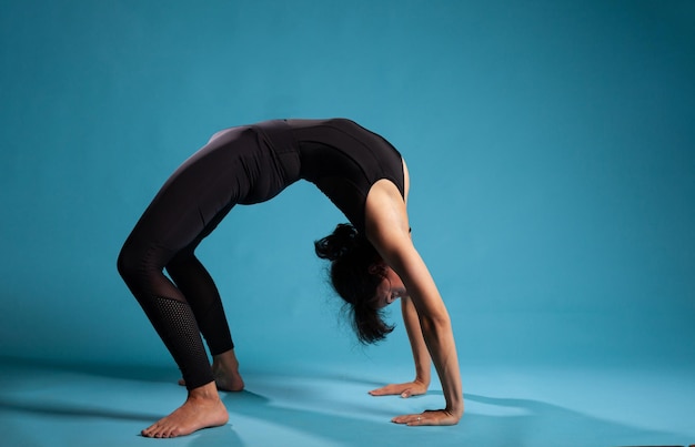 Personal Trainer üben urdhva dhanurasana Übungsstudio mit blauem Hintergrund. Fitte aktive Person, die Körpermuskeln dehnt, die an einem gesunden Lebensstil arbeiten. Bridge-Pose-Konzept