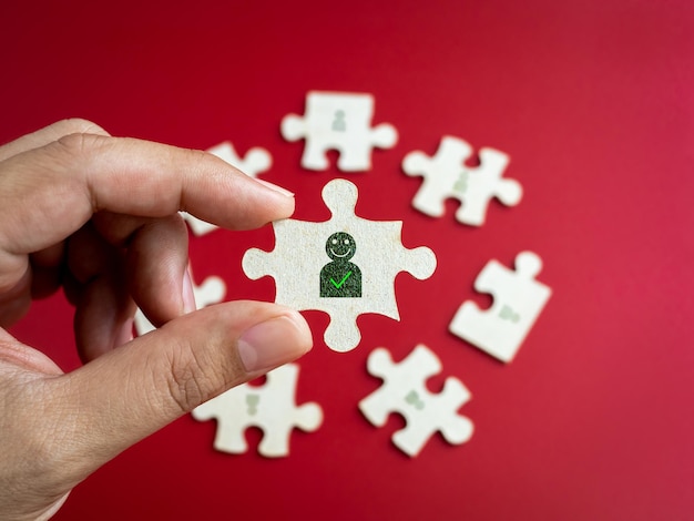 Personal- und Managementteamauswahl Geschäftsleute Beziehungskonzepte Menschen-Symbol mit Häkchen-Symbol auf einem Puzzle-Puzzle, das an der Hand des Menschen mit anderen Teilen auf rotem Hintergrund gehalten wird