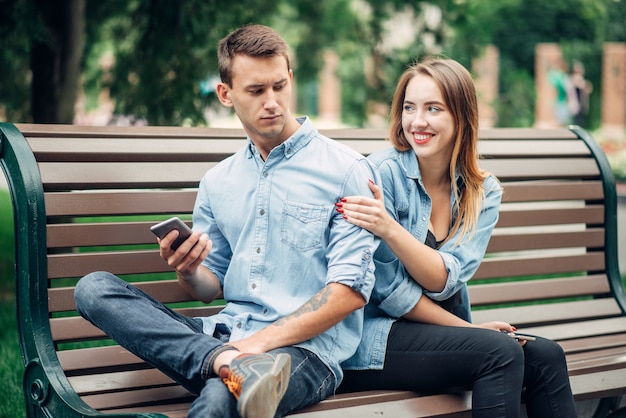 Personas adictas al teléfono, hombre con smartphone e ignorando a su mujer, pareja en el parque de verano, adicto social