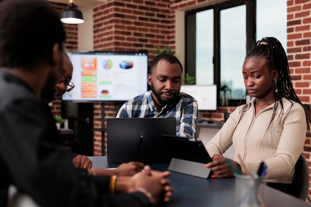 Personas afroamericanas intercambian ideas en reuniones, usan computadoras portátiles y tabletas para crear presentaciones en línea con investigación de datos e información. Análisis de documentos y archivos para enviar informes por correo electrónico.