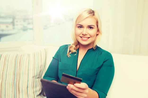 personas, banco de Internet, compras en línea, tecnología y concepto de dinero electrónico - mujer joven feliz sentada en un sofá con computadora de tablet pc y tarjeta de crédito en casa