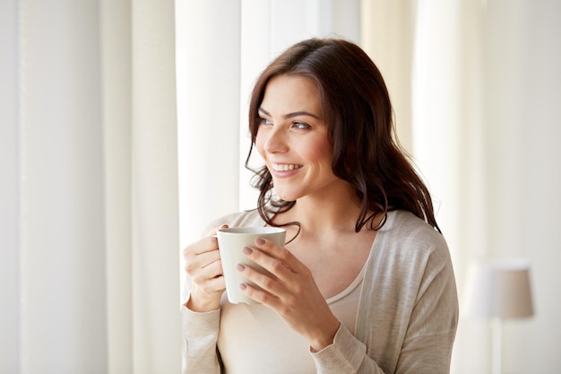 personas, bebidas y concepto de ocio - mujer joven feliz con una taza de té o café en casa