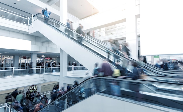 Personas borrosas usando una escalera mecánica en una Feria Comercial Internacional