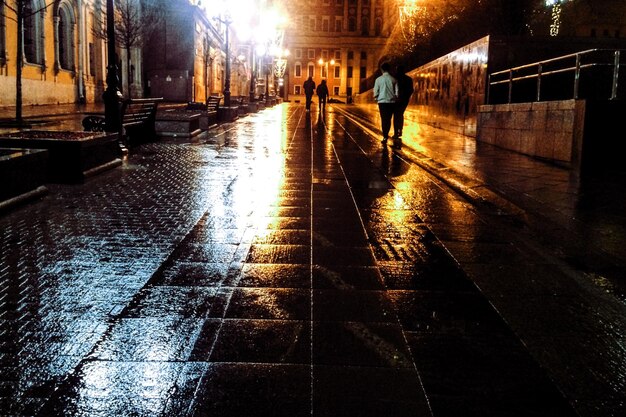 Foto personas caminando por la calle húmeda iluminada por la noche