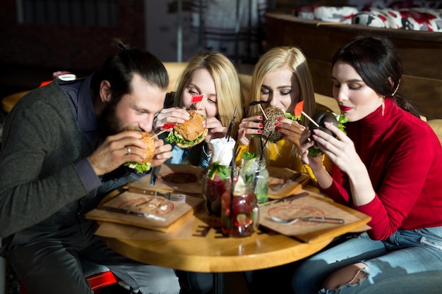 Las personas cenan juntas en una mesa en un café. Amigos felices comen hamburguesas y se divierten.