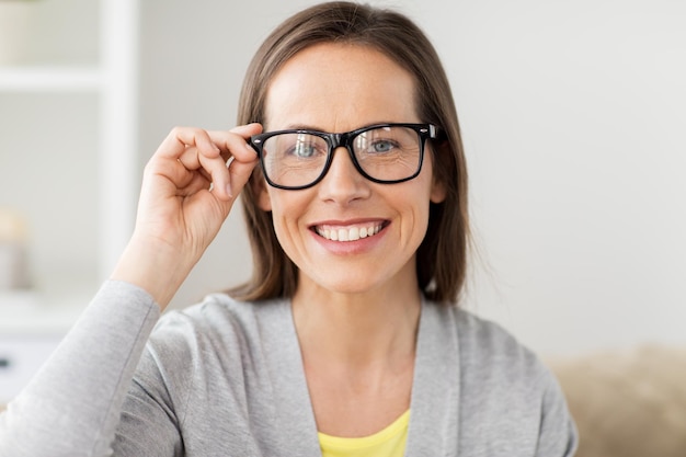 Foto personas y concepto de visión - feliz sonriente mujer de mediana edad con gafas en casa