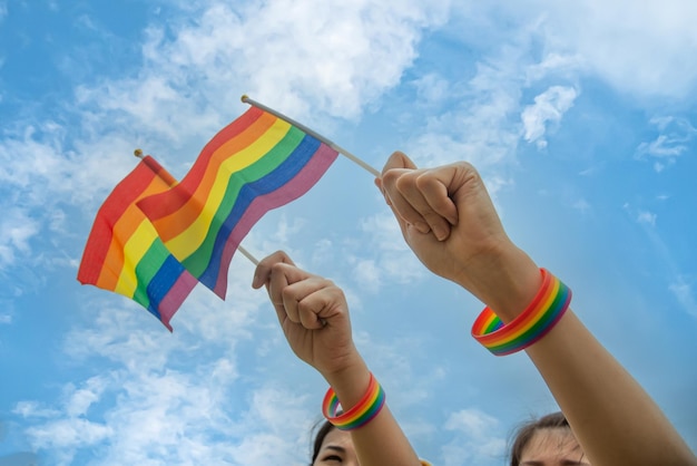 Personas de la diversidad manos levantando coloridas banderas del arco iris lgbtq juntas y usan Rocket Wristband LGBT