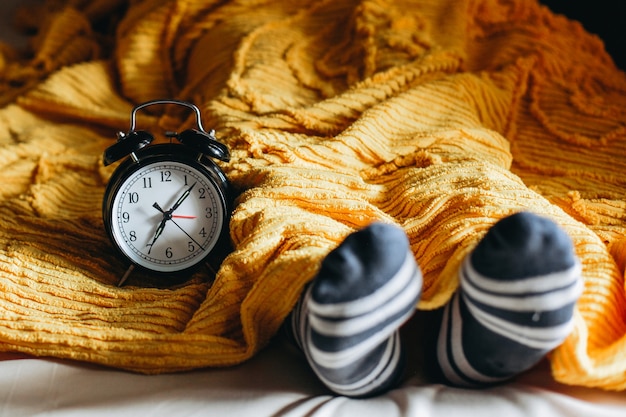 Personas durmiendo en una cama debajo de las mantas y calcetines calientes con reloj despertador que muestra las 7 en el lateral