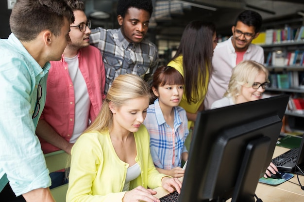 personas, educación, tecnología y concepto escolar - grupo de estudiantes internacionales felices y sonrientes con computadoras en la biblioteca de la universidad