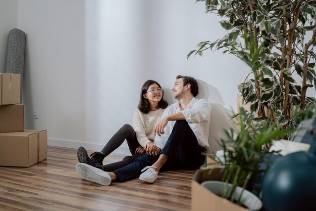 Las personas enamoradas están sentadas apoyadas contra la pared en un apartamento recién comprado, un hombre con una camisa elegante