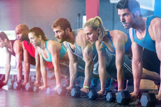 Personas haciendo flexiones con mancuernas en el gimnasio