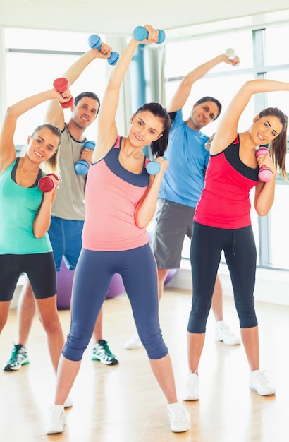 Personas levantando pesas con mancuernas con el entrenador en el gimnasio