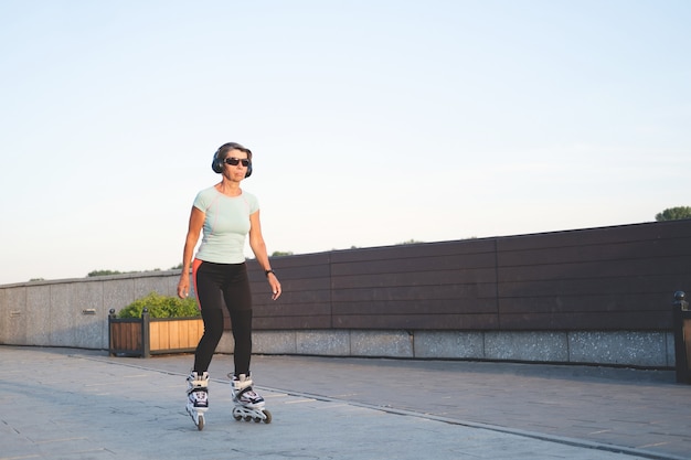 Personas mayores activas mujer caucásica patinar en la ciudad al aire libre. escuchar música. Auriculares. Estilo de vida saludable. Aptitud física. terraplén. Foto de alta calidad