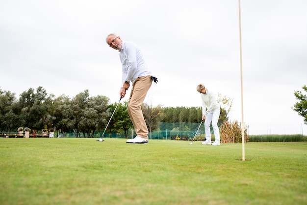 Personas mayores activas que se divierten en el campo de golf y disfrutan del tiempo libre al aire libre.