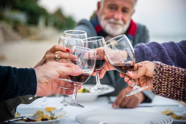 Personas mayores brindando con vino tinto en la playa