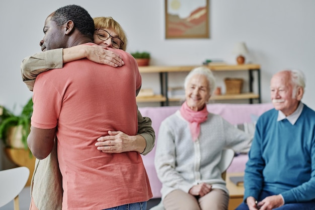 Personas mayores felices de verse, de pie en la habitación y abrazándose