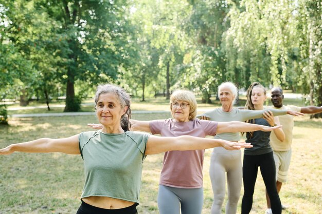 Foto personas mayores paradas en fila y haciendo ejercicios junto con el entrenador al aire libre