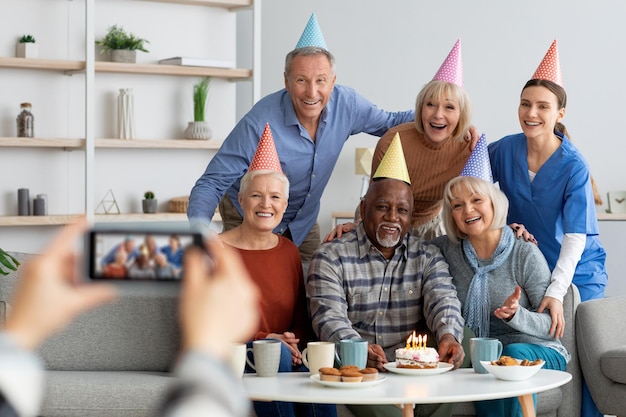 Personas mayores positivas y enfermeras celebrando cumpleaños tomando fotos