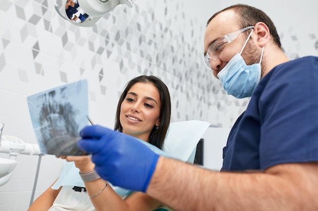 Foto personas medicina estomatología y concepto de atención médica dentista masculino feliz mostrando el plan de trabajo a la paciente mujer en la oficina de la clínica dental