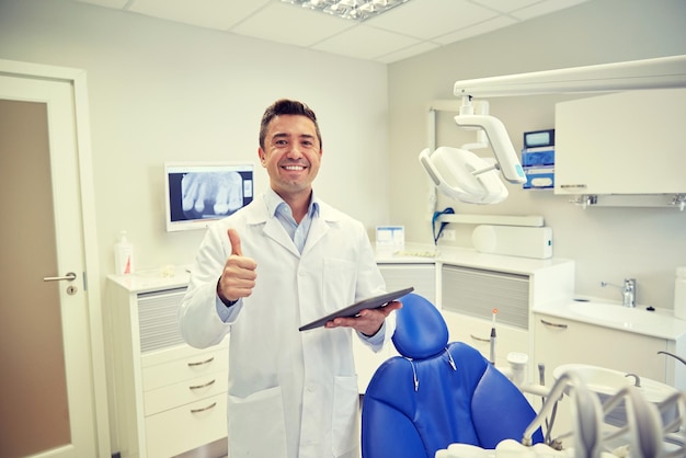 personas, medicina, estomatología y concepto de atención médica - feliz dentista masculino de mediana edad con bata blanca con computadora de tablet pc que muestra los pulgares hacia arriba en la oficina de la clínica dental