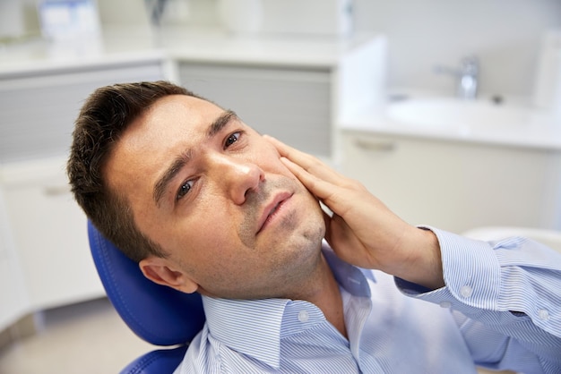 personas, medicina, estomatología y concepto de atención médica - paciente varón infeliz con dolor de muelas sentado en una silla dental en la oficina de la clínica