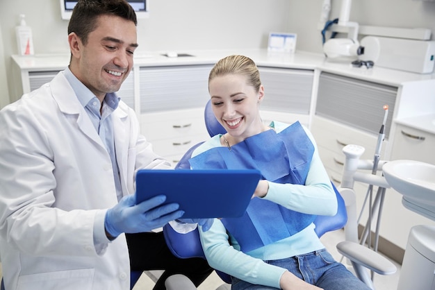 personas, medicina, estomatología y concepto de atención de la salud - dentista masculino feliz que muestra una computadora de tablet pc a una paciente en la oficina de la clínica dental