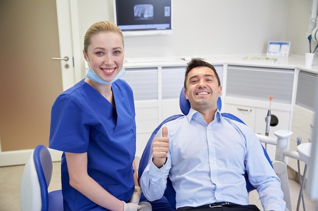 personas, medicina, estomatología, gestos y concepto de atención de la salud - dentista feliz con un paciente que muestra su aprobación en la oficina de la clínica dental