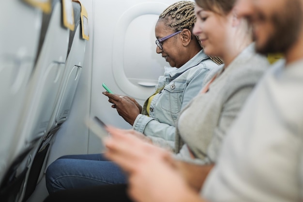 Personas multirraciales sentadas dentro del avión mientras usan el teléfono móvil