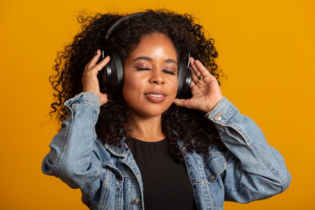 Personas, música, concepto de emociones. Encantadora mujer despreocupada con peinado afro baila al ritmo de la melodía, cierra los ojos y escucha una canción ruidosa en los auriculares. Hermosa mujer afro con sus auriculares