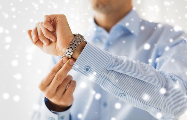 Foto personas, negocios, accesorios y concepto de ropa - cierre de un hombre con un reloj de pulsera en casa sobre el efecto de la nieve