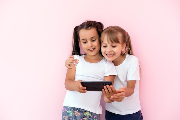 personas, niños, tecnología, amigos y concepto de amistad: niñas felices con teléfonos inteligentes tirados en el suelo en la educación en el hogar, la escuela está usando un teléfono inteligente y sonriendo