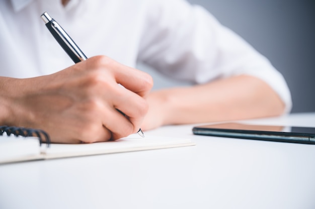 Personas que escriben en el cuaderno y trabajan con papel en la mesa de madera.