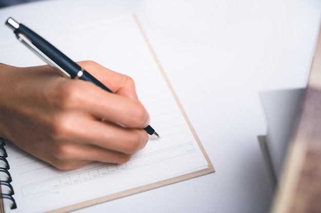 Personas que escriben en el cuaderno y trabajan con papel en la mesa de madera.