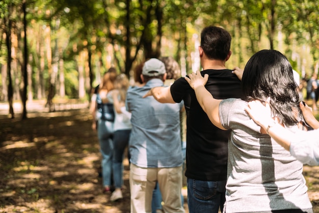 Foto las personas que realizan ejercicios de formación de equipos se paran una detrás de la otra y sostienen sus hombros con las manos hacia atrás