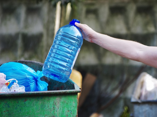 Personas que sostienen la botella de basura de plástico y vidrio colocándola en una bolsa de reciclaje para limpiarla
