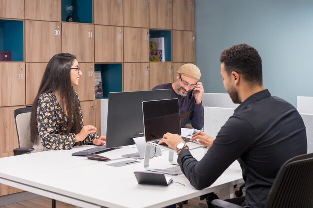 Personas que trabajan con computadoras portátiles y hablan por teléfono en un escritorio de coworking