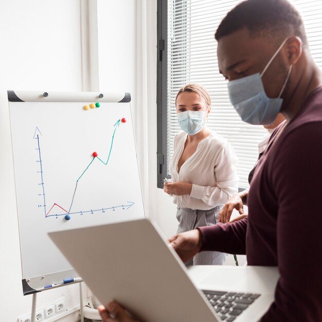 Personas que trabajan en la oficina durante la pandemia con máscaras médicas y son productivas