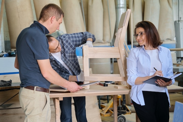 Personas que trabajan en el taller de carpintería, trabajadores de mujeres y hombres que hacen una muestra de silla de madera con dibujo de diseño