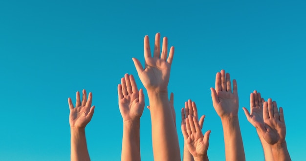 Personas rasing manos sobre fondo de cielo azul. Concepto de voto, democracia o voluntariado